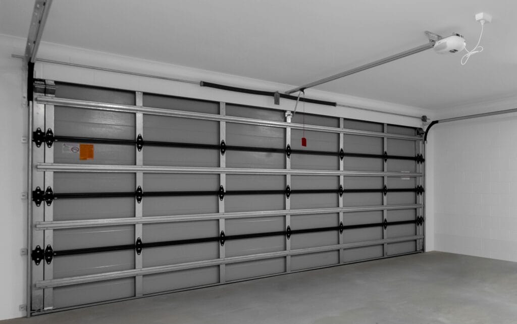 Internal view of a sectional garage door's hardware, including the track, rollers, and panel hinges. - Gliderol